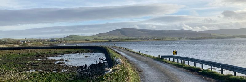 Irish countryside — a road through a lake with mountains in the background.
